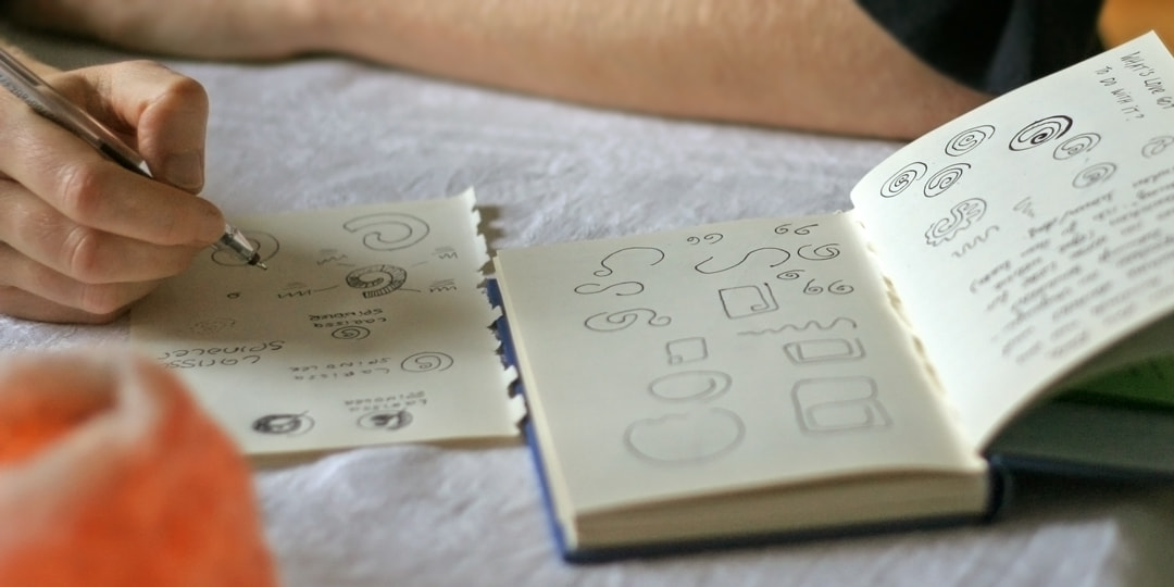 Larissa zeichnet Skizzen für ihr Logo in ein Notizbuch